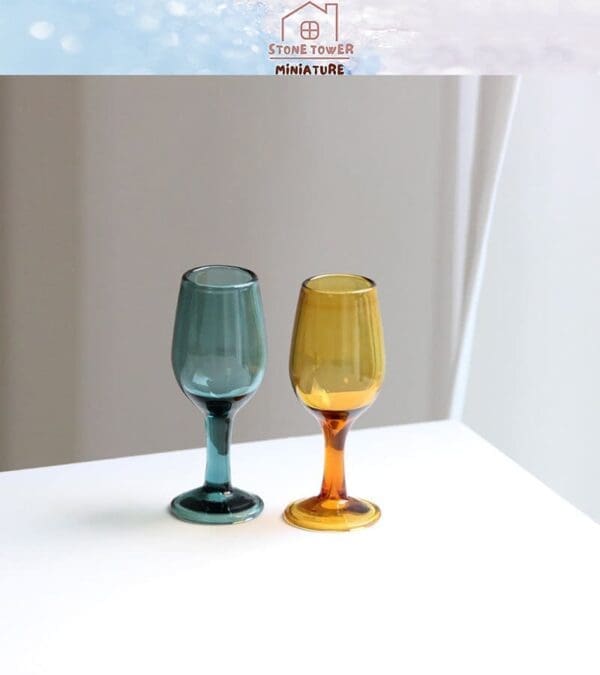 Two miniature wine glasses, one teal and one amber, on a white surface with a soft background.