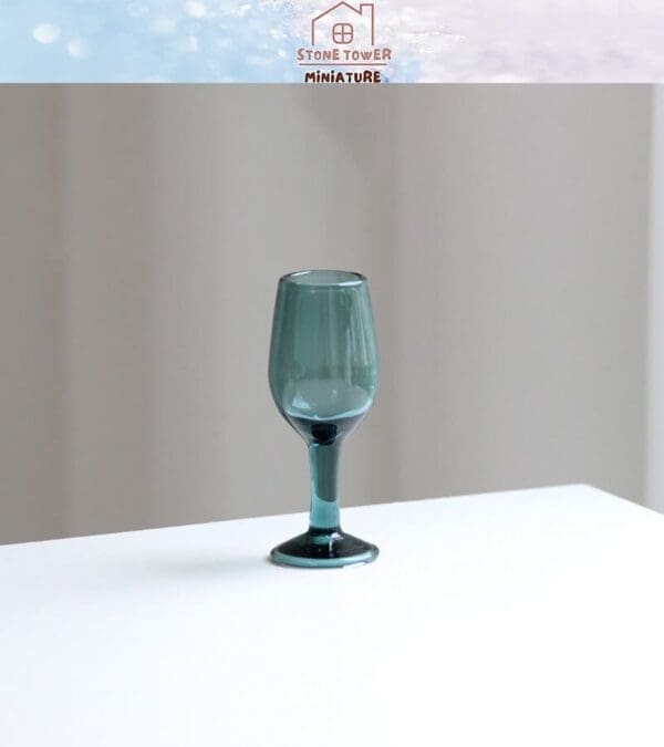 Dark green miniature wine glass on a white surface with a blurred background.