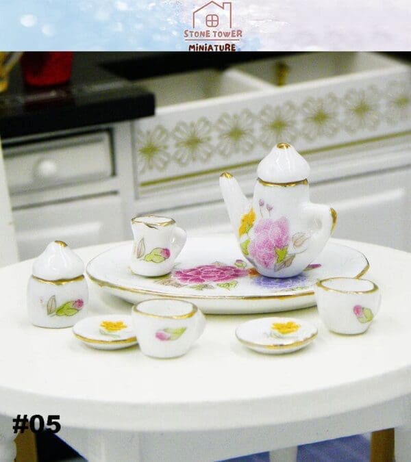 Miniature porcelain tea set with floral designs on a white table. Features teapot, cups, saucers, and a sugar bowl.