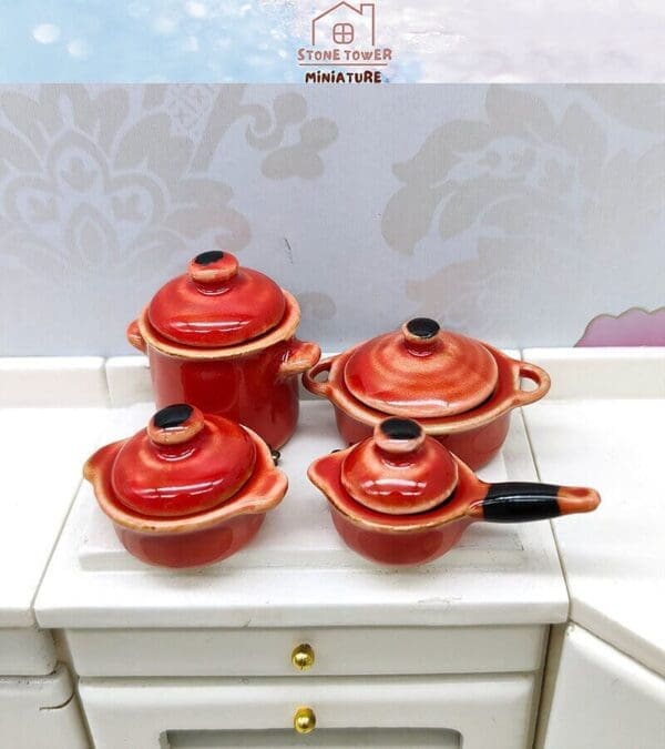 Set of four red miniature kitchen pots with lids on a white countertop.