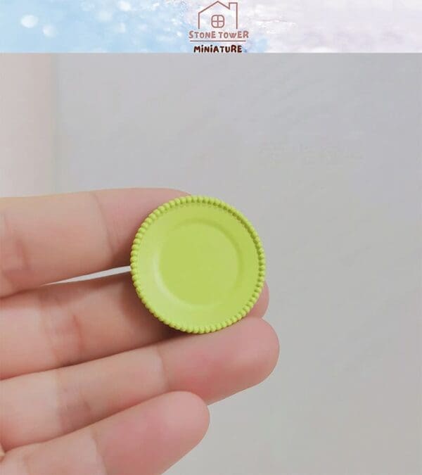 Hand holding a small, green, round miniature plate with a textured edge.