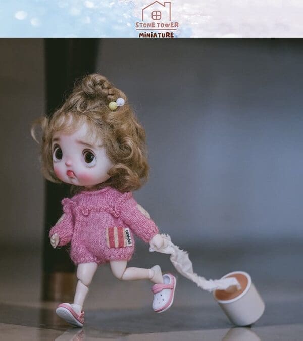 Cute doll in pink sweater running with toilet paper roll, background blurred, Stone Tower Miniature logo above.