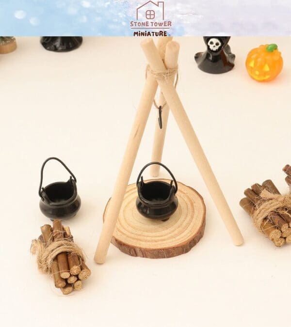 Miniature campsite setup with wooden sticks, a tripod stand, and small black cauldrons on a slice of log.