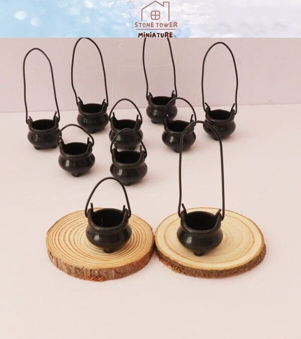 Nine miniature black cauldrons with handles, two on wooden slices, arranged on a white surface.