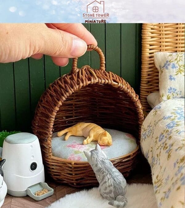 Miniature wicker pet bed with a sleeping orange cat figurine, a gray cat figure, and a smart feeder nearby.