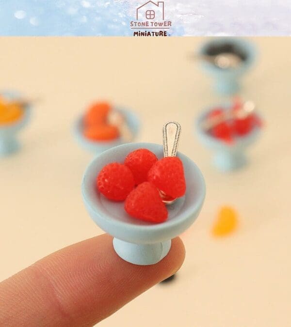 Miniature blue dish with red berries and a tiny spoon, balancing on a fingertip.