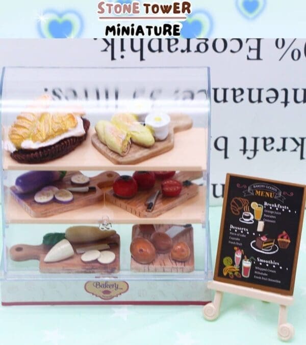 Miniature bakery display with croissants, vegetables, and bread next to a chalkboard menu on an easel.