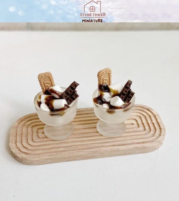 Two miniature dessert cups with chocolate, cookies, and marshmallows on a wooden tray.