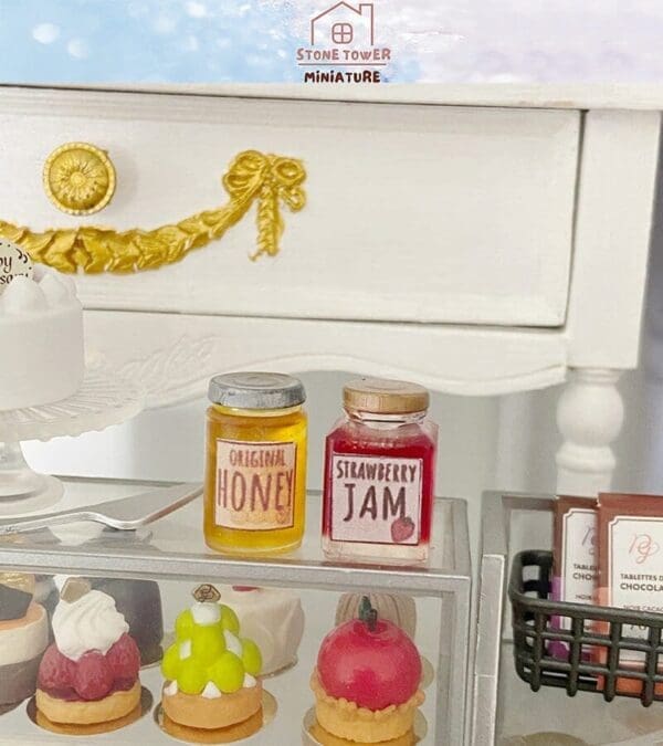 Miniature jars of honey and strawberry jam displayed near tiny desserts on a decorative shelf.