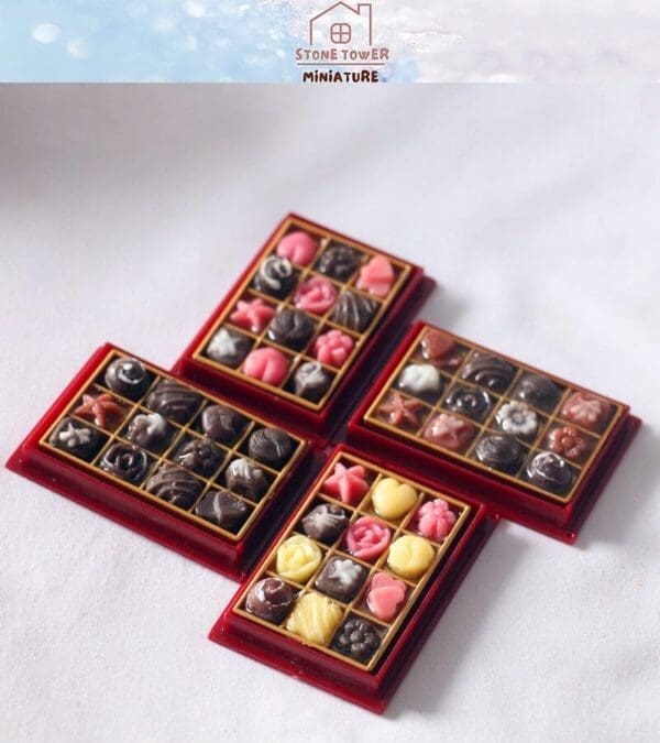 Four trays of assorted miniature chocolates with various designs in red boxes on a white surface.