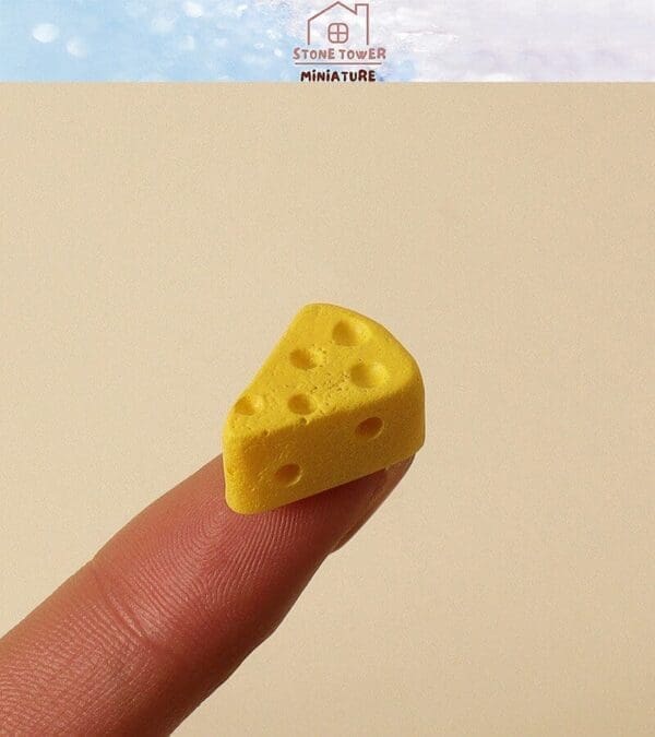 Miniature yellow cheese slice with holes, balanced on fingertip against beige background.