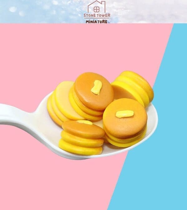 Miniature pancakes with butter on a spoon, set against a pink and blue background.