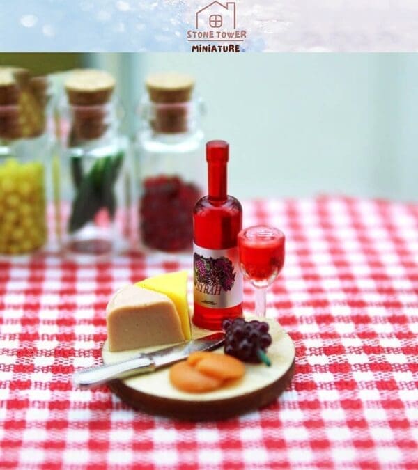 Miniature picnic set with wine, cheese, grapes, and a knife on a checkered tablecloth.