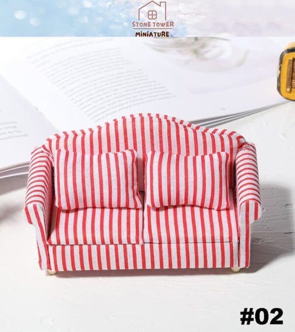 Miniature red and white striped sofa with two cushions on a white surface, near an open book.