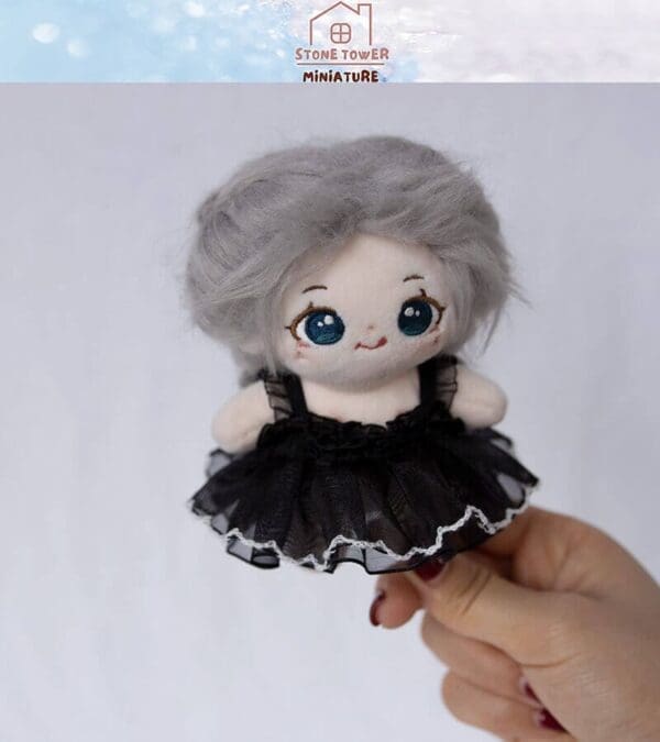 Plush doll with gray hair in black dress held by a hand against a plain background. Stone Tower Miniature logo above.