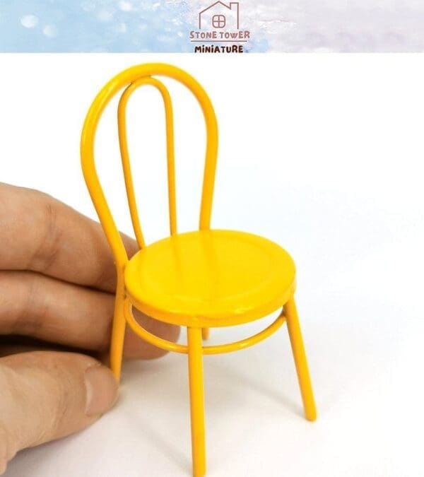 A hand holding a small yellow miniature chair with a simple curved backrest on a white background.