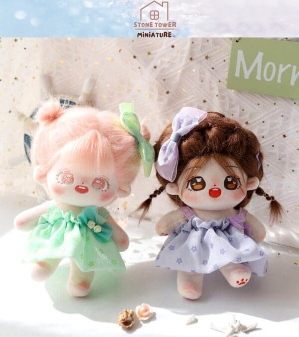 Two cute plush dolls with colorful dresses and bows are displayed, surrounded by small seashells and a starfish.