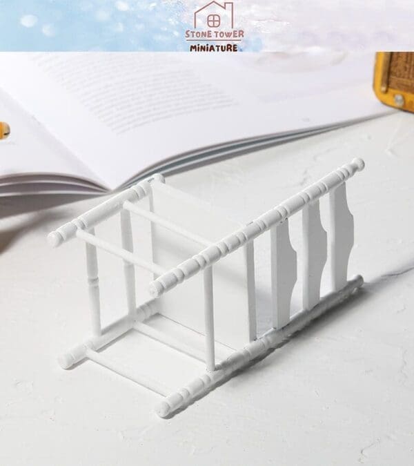 White miniature towel rack on a white surface with an open book in the background.