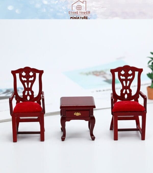 Two miniature red wooden chairs with red cushions flank a small wooden table on a white surface.