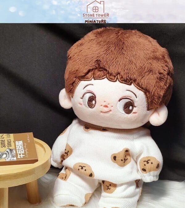 Cute plush doll with brown hair in a bear-patterned outfit, sitting on a white surface next to a small wooden table.