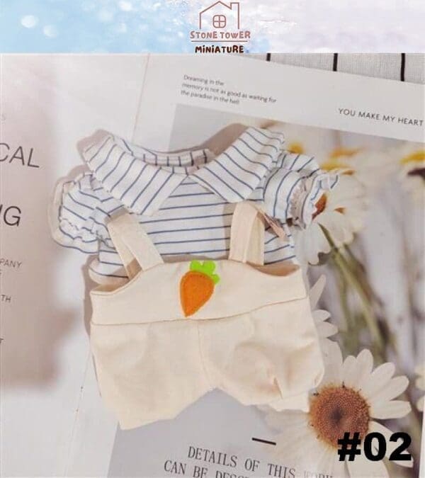 Striped baby outfit with carrot-appliqué suspenders laying on an open book with daisies around.