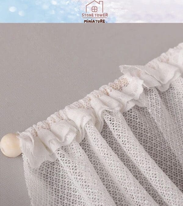 White lace curtain with gathered top on a beige rod, under the brand Stone Tower Miniature logo on a light background.