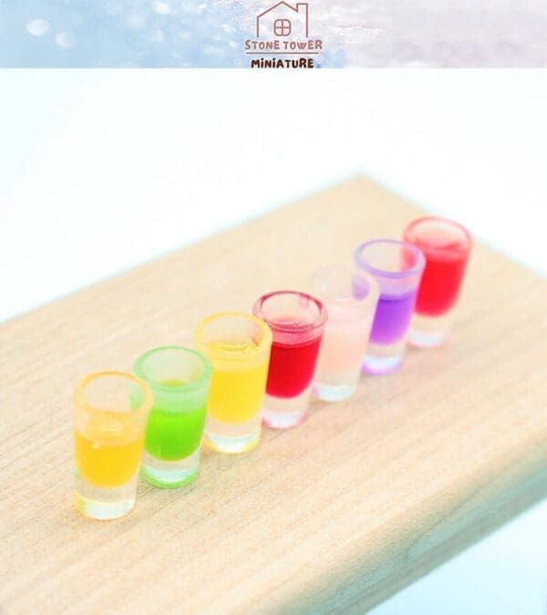 Colorful miniature drinks in six shot glasses on a wooden surface.