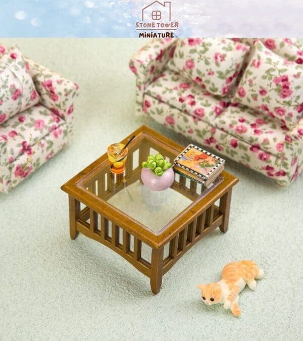 Miniature living room with floral sofas, a wooden coffee table, books, a drink, and a small cat figure on the floor.