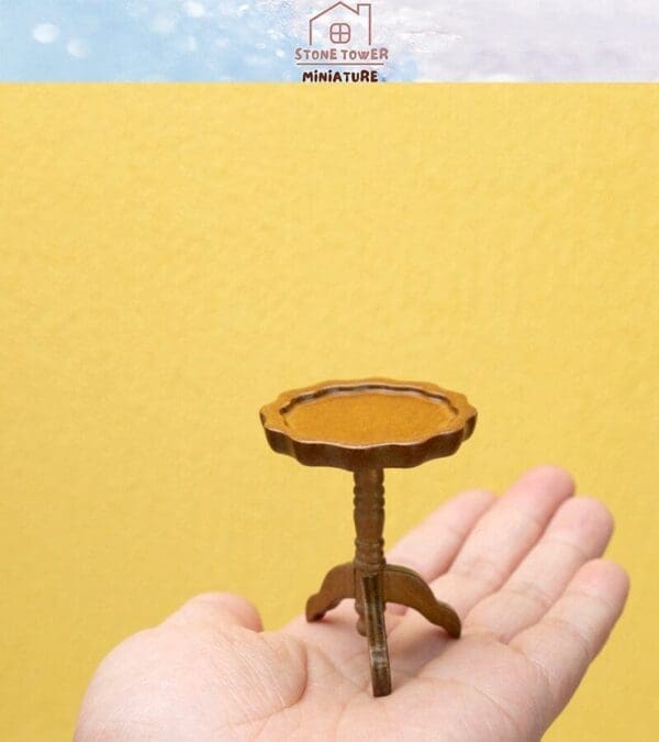 A small, brown miniature table held in a hand against a yellow background, with "Stone Tower Miniature" printed above.