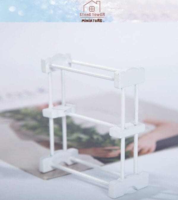 White miniature drying rack on a blurred magazine background with a "Stone Tower Miniature" logo at the top.