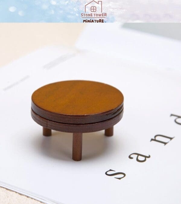 Miniature wooden round table on a textured white surface with a blurred background.