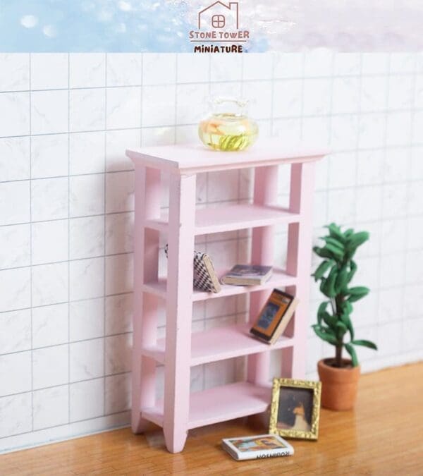 Pink miniature bookshelf with books and a vase. A small plant and picture frame are on the wooden floor.