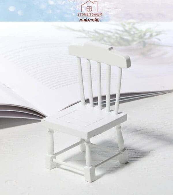 Miniature white chair placed on an open book, with soft lighting and a blurred plant in the background.