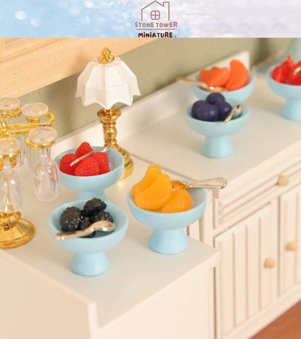 Miniature fruit bowls and drinks on a white countertop with small decorative lamp.