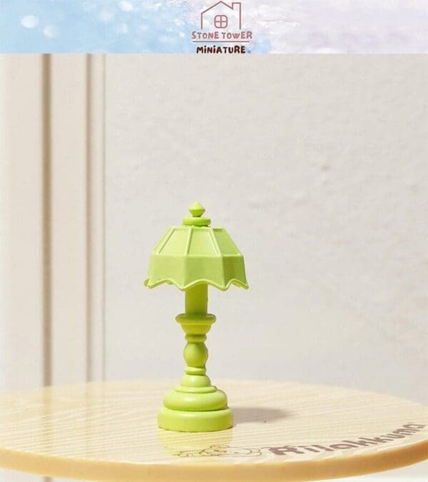 Miniature green table lamp with a decorative shade on a light wooden surface.