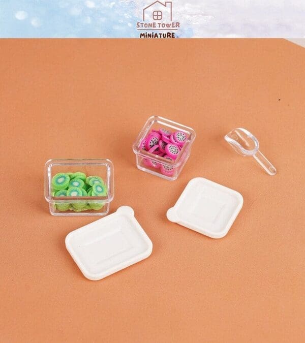 Miniature containers with kiwi and dragon fruit slices, lids, and a clear scoop on a brown surface.