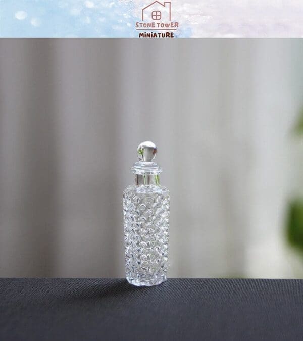 A clear, textured miniature glass bottle with a round stopper on a dark surface, against a blurred background.