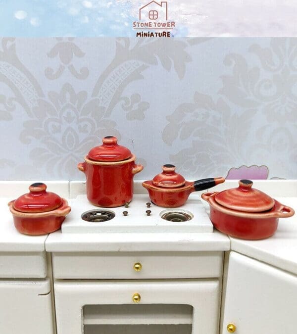 Miniature red cookware set on a white toy kitchen counter with decorative wallpaper background.