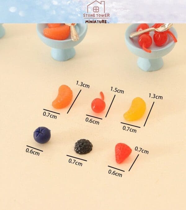 Miniature fruit models on a table with size measurements, including orange slices, cherries, and berries.