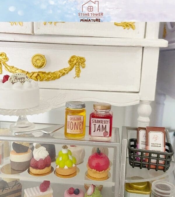 Miniature display with dessert pastries, jars of honey and jam, and a white cake on a decorative stand.