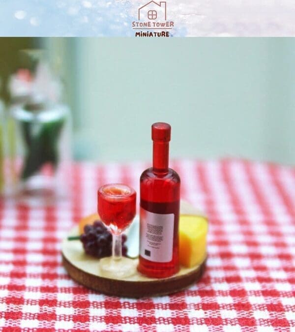 Miniature wine bottle and glass with cheese and grapes on red-checkered tablecloth.