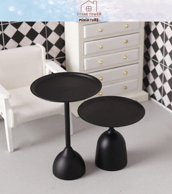 Two black miniature tables in a dollhouse setting with a white chair and checkered wall in the background.