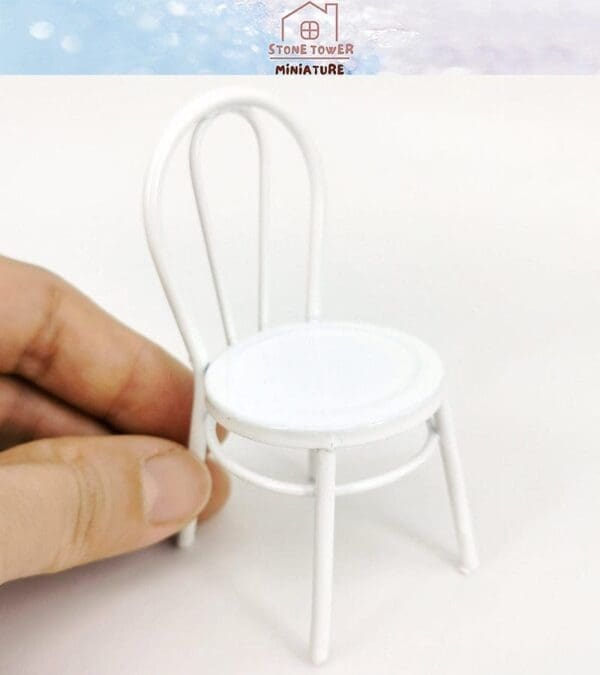 Hand holding a small white metal miniature chair on a white background.