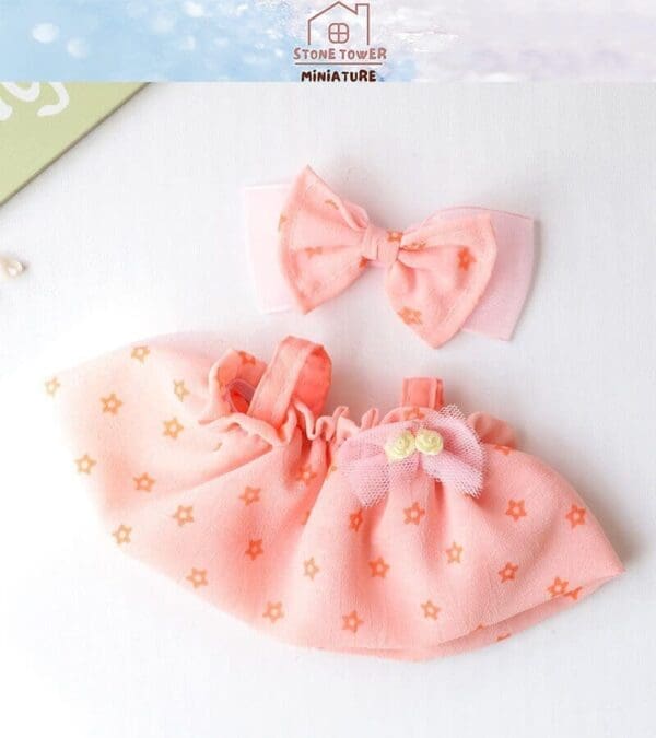 Pink doll dress with orange star pattern and bow embellishment, paired with matching hair bow on a white background.