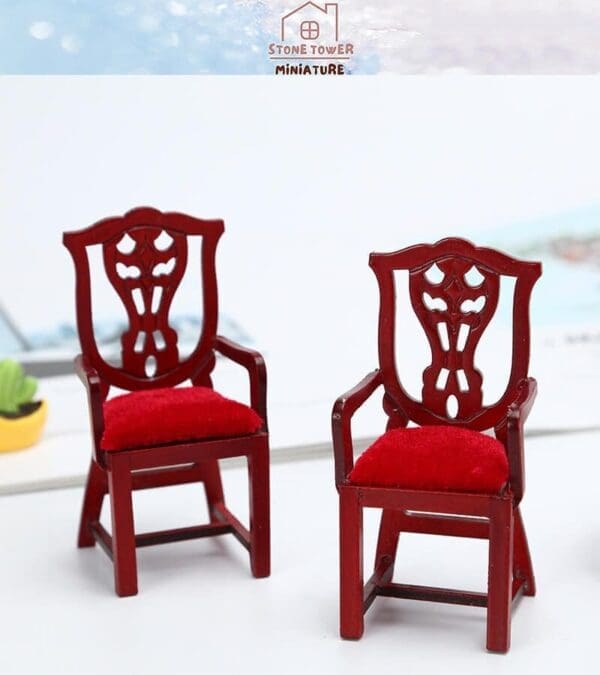 Two ornate red wooden miniature chairs with red cushioned seats on a white surface.