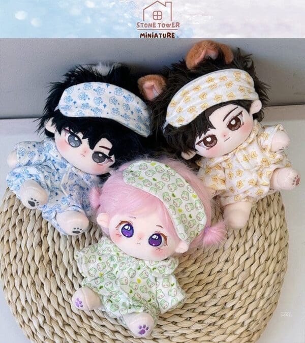 Three cute plush dolls with sleep masks and pajamas sit on a woven mat; one pink-haired, one with black hair, one with ears.