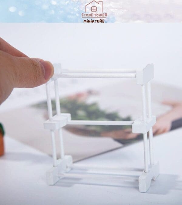 Hand holding a small white plastic rack above a blurred background with "Stone Tower Miniature" text.