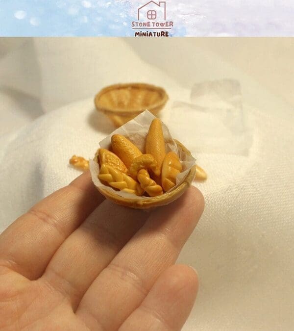 Hand holding a tiny basket of miniature breads on a white background.