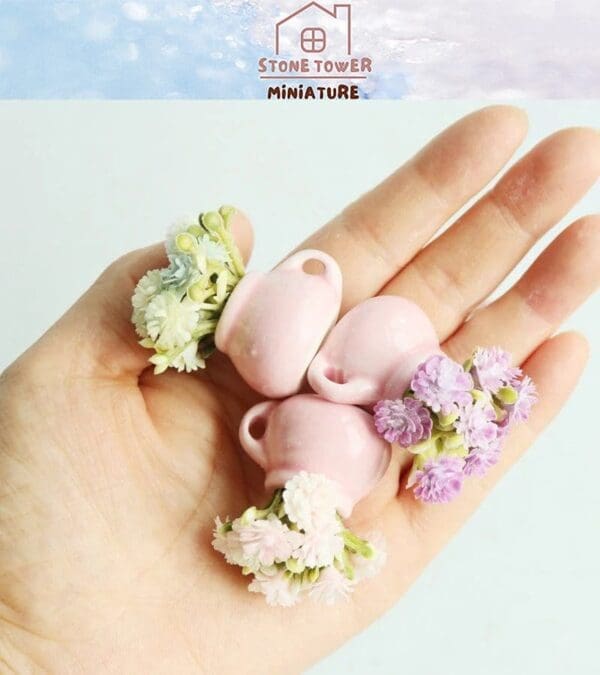 Hand holding small pink vases with delicate pastel flowers, showcasing miniature craftsmanship.