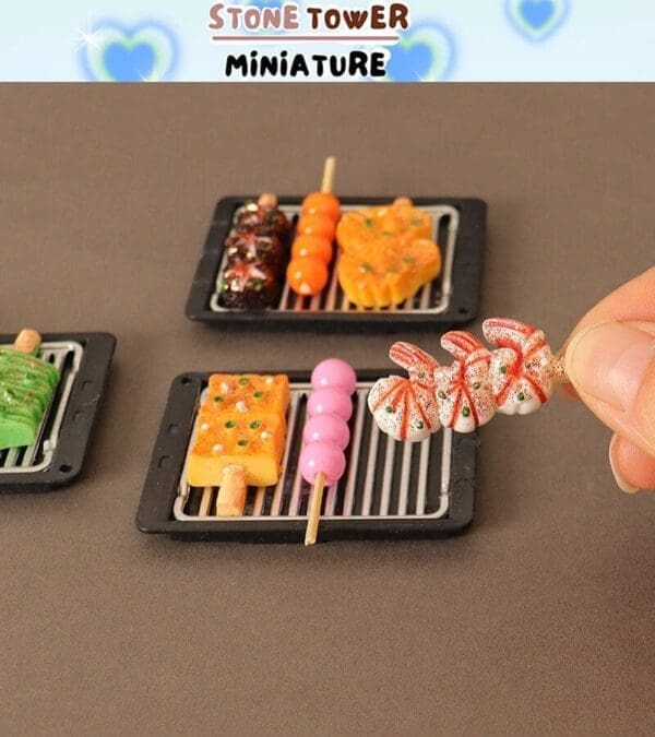 Miniature skewers on grills, featuring colorful faux food art, held by a hand on a brown background.